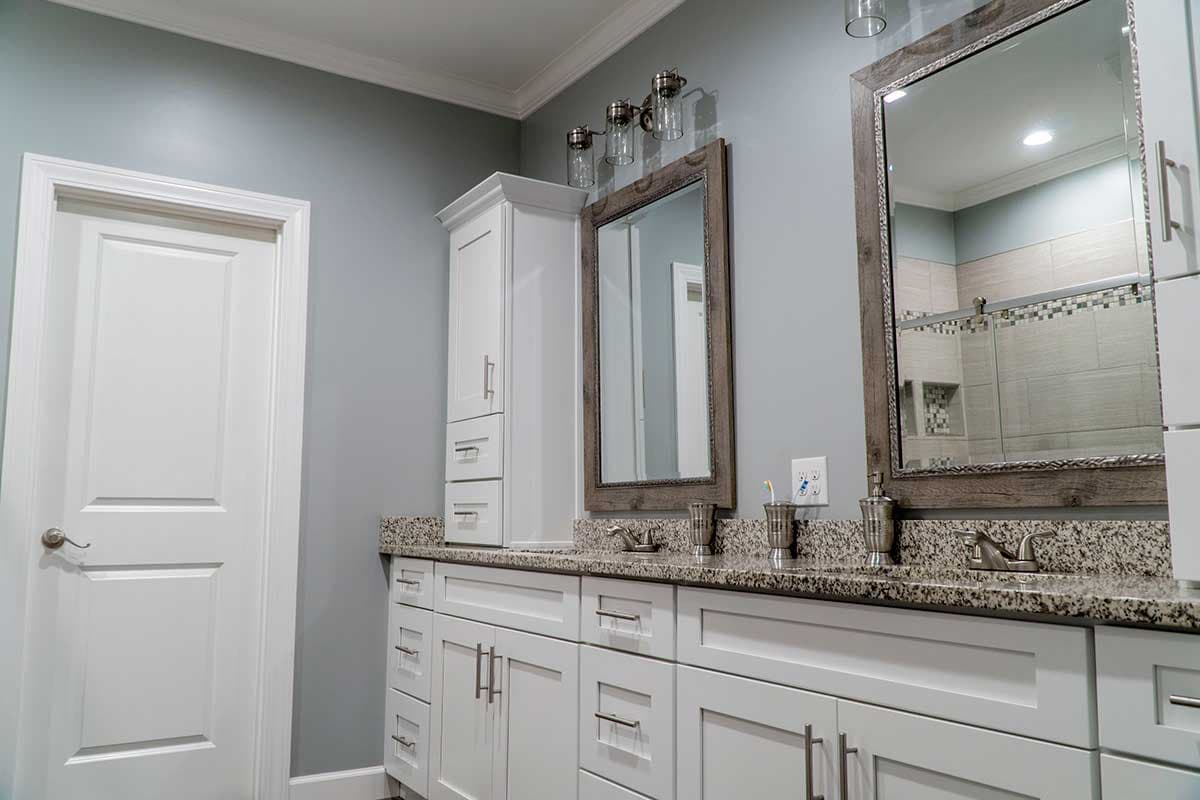 Bathroom interior with double vanity, granite countertops, white cabinetry, and a glass-enclosed shower.