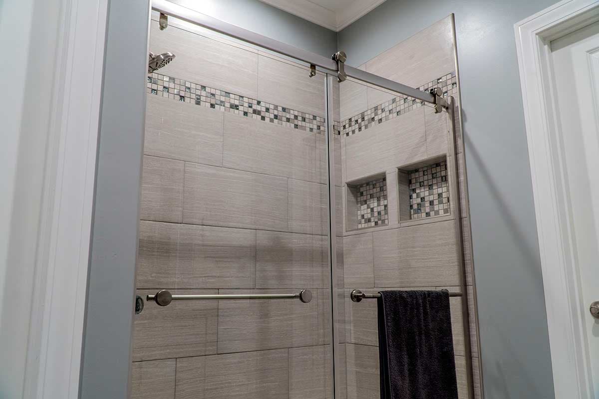 Modern bathroom with tiled shower, sliding glass door, shower niches, and brushed nickel fixtures.