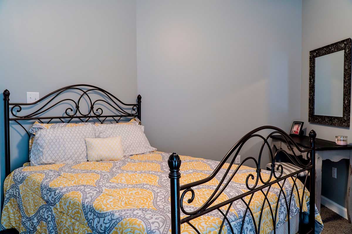 Bedroom with metal bed frame, patterned comforter, and decorative mirror on a console table.