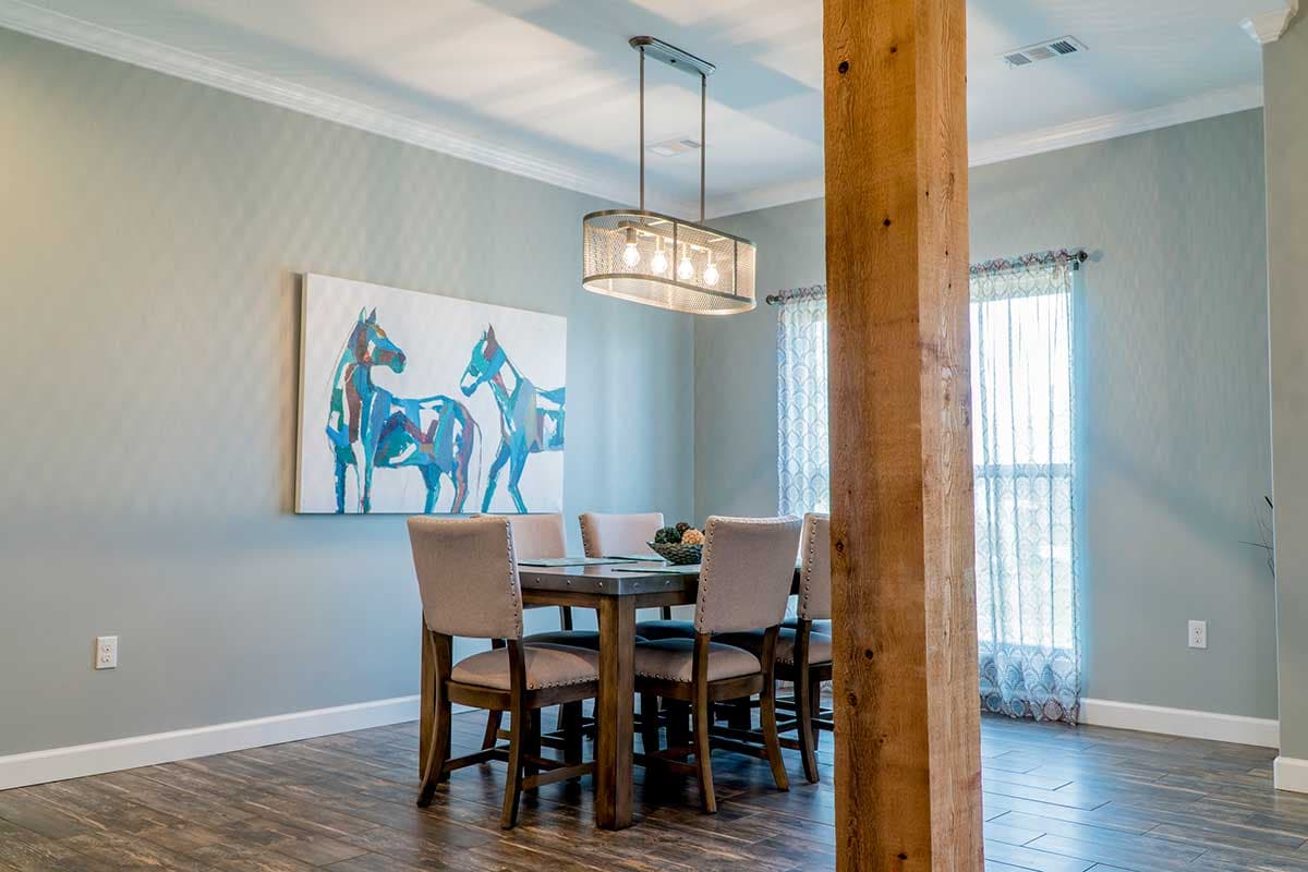 Dining room with a wooden table, upholstered chairs, contemporary art, and a rustic wood pillar.