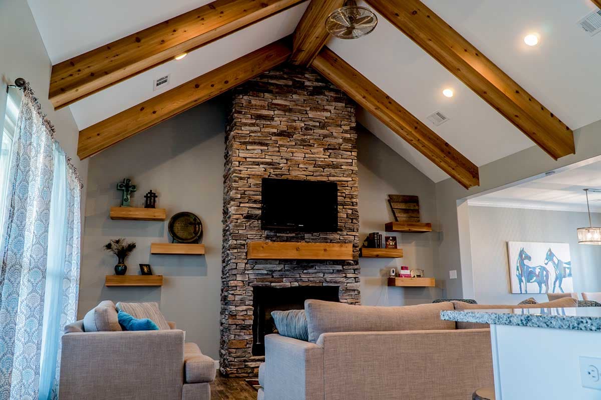 Interior view of living room with vaulted ceiling, exposed wooden beams, and a floor-to-ceiling stone fireplace.