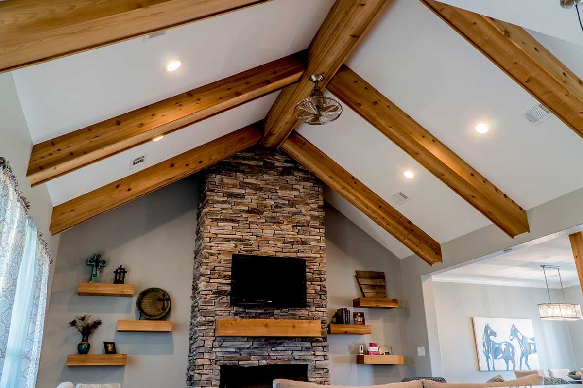 Interior view of great room with vaulted ceiling, exposed wooden beams, and stone fireplace with television.