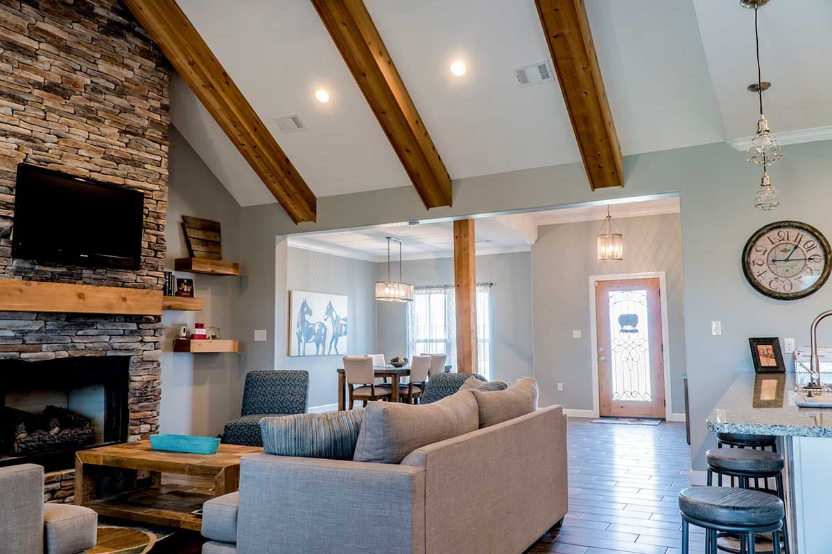 Great room with vaulted ceiling, exposed beams, stone fireplace, and open view to dining area and entryway.