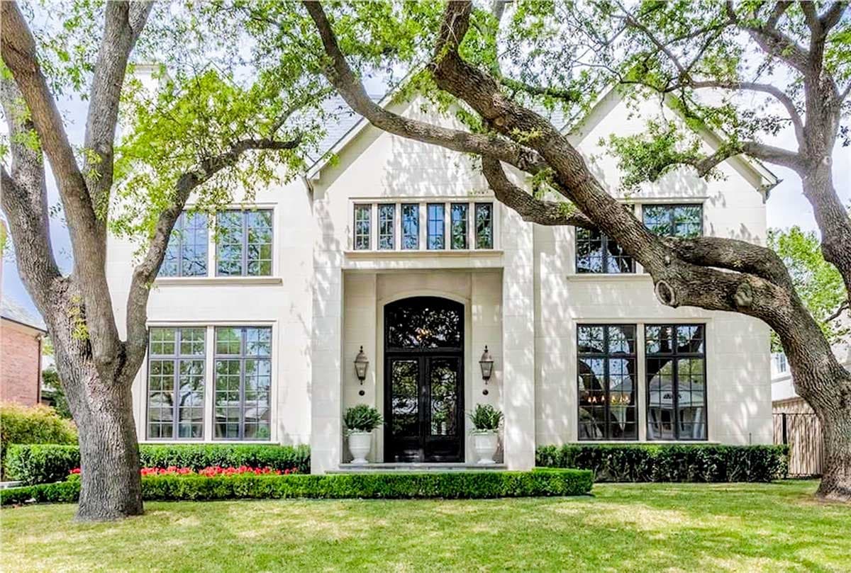House plan exterior. Two-story home with symmetrical facade, large windows, and a portico with a black, arched door. Mature trees frame the view.
