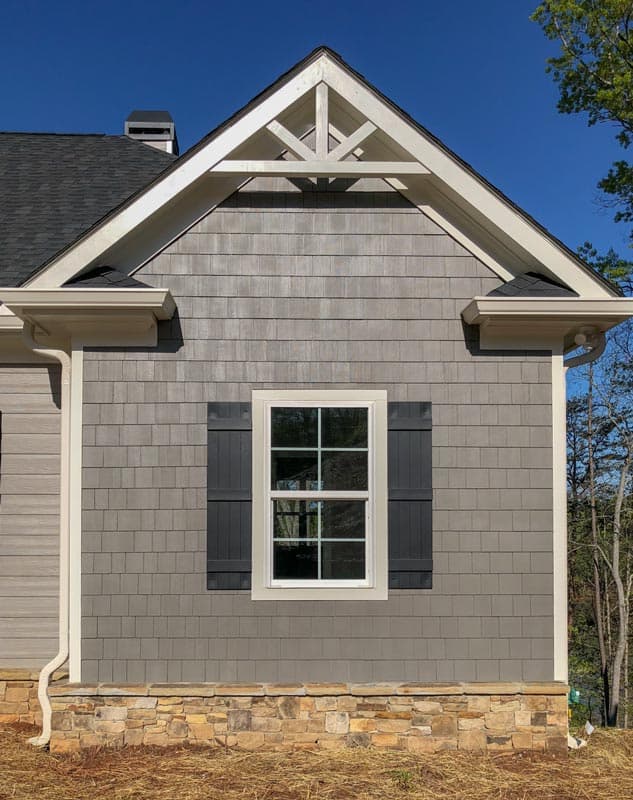House plan exterior detail: Gable with decorative rafter tails, shingle siding, stone foundation, and window with dark shutters.