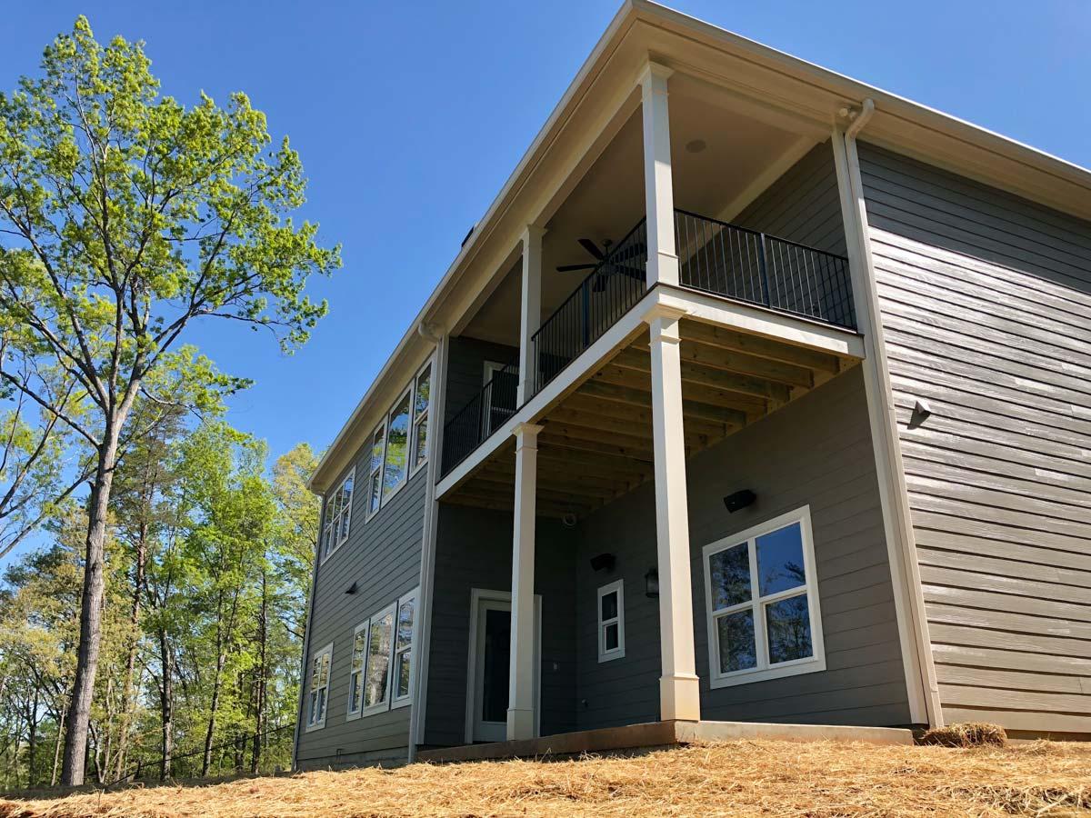Two-story house plan exterior with double-level covered porch, dark railing, and horizontal siding.