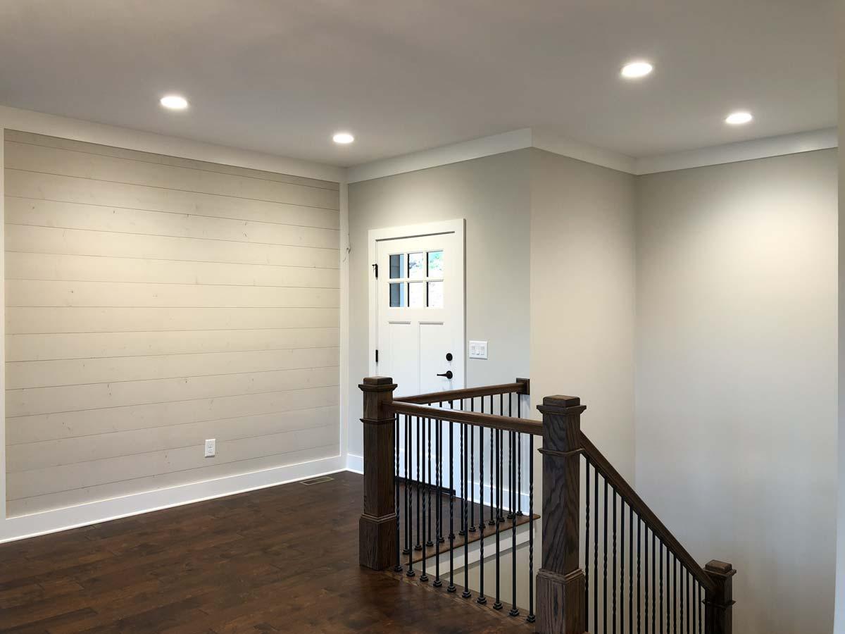 Interior view showing a shiplap accent wall, a staircase with dark wood railings, and a white paneled door with glass.