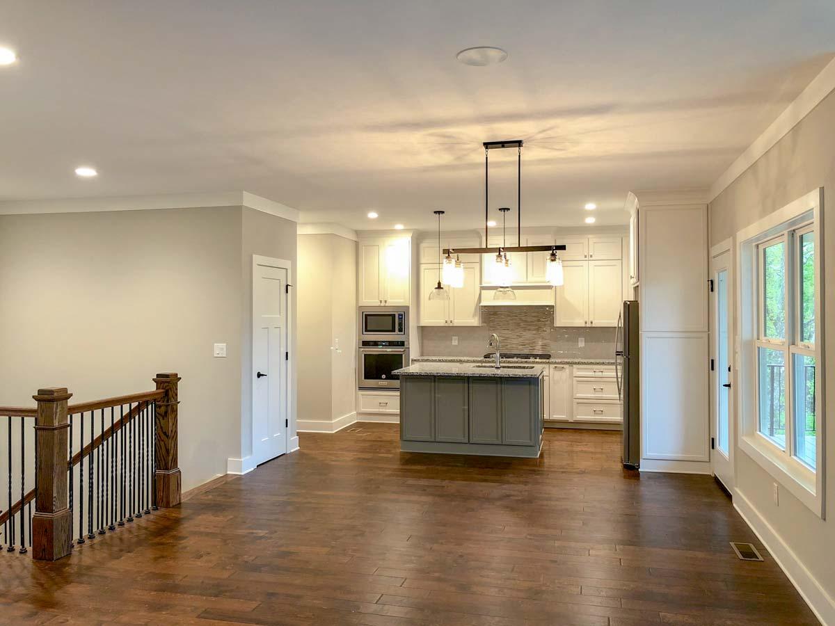 Open-concept kitchen with central island, white cabinetry, stainless steel appliances, and adjacent living area with staircase.