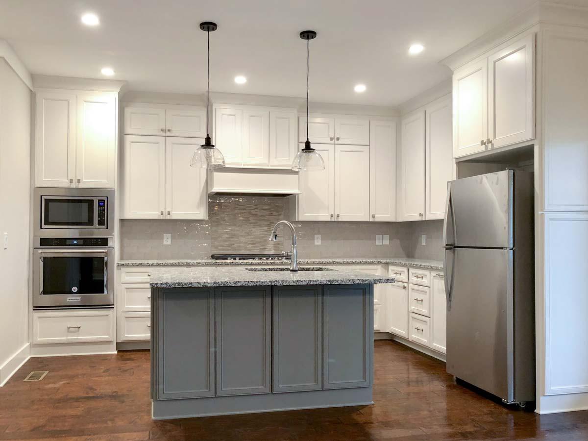 Kitchen with white cabinets, granite countertops, gray island, stainless steel appliances, and mosaic tile backsplash.