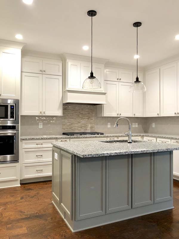 Kitchen interior with white cabinetry, a grey island with granite countertop, pendant lights, and stainless steel appliances.