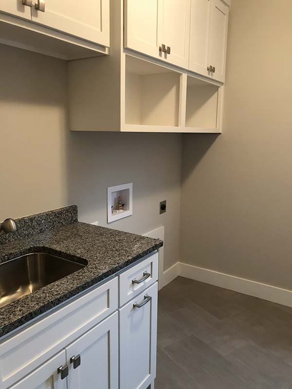 Laundry room with white cabinets, granite countertop, sink, and stacked washer/dryer hookups.