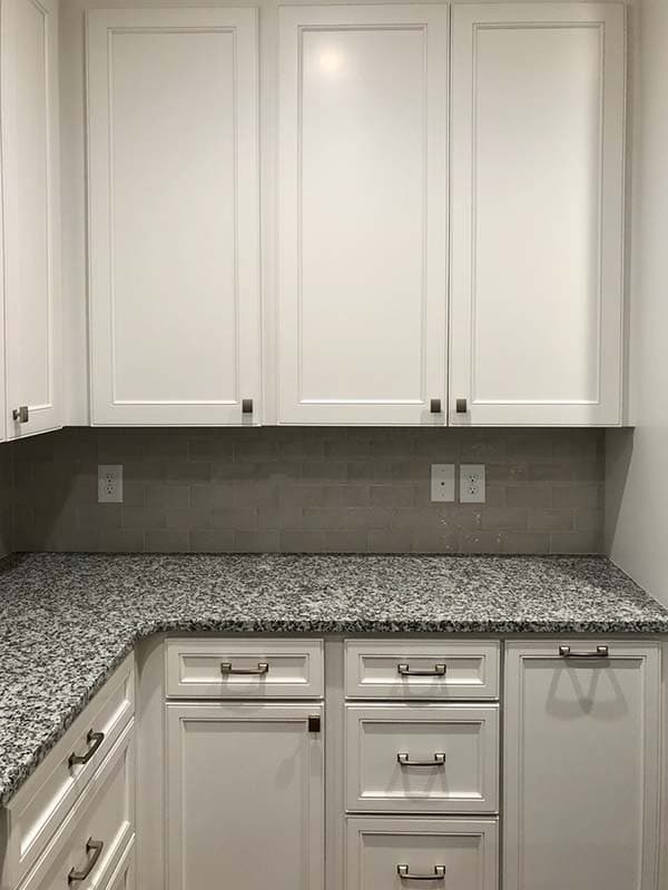 Kitchen cabinetry with white shaker doors, granite countertops, and a gray subway tile backsplash.