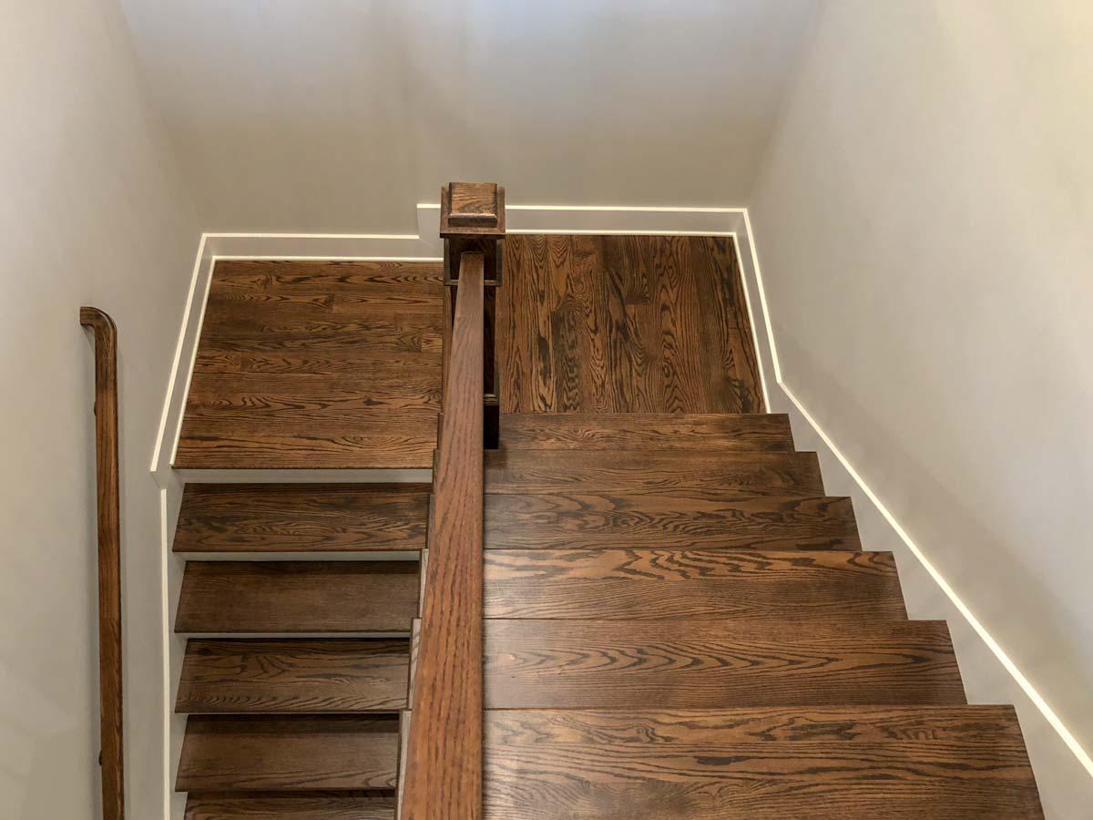 Interior staircase with dark wood treads and risers, wooden handrail, and minimalist accent lighting.