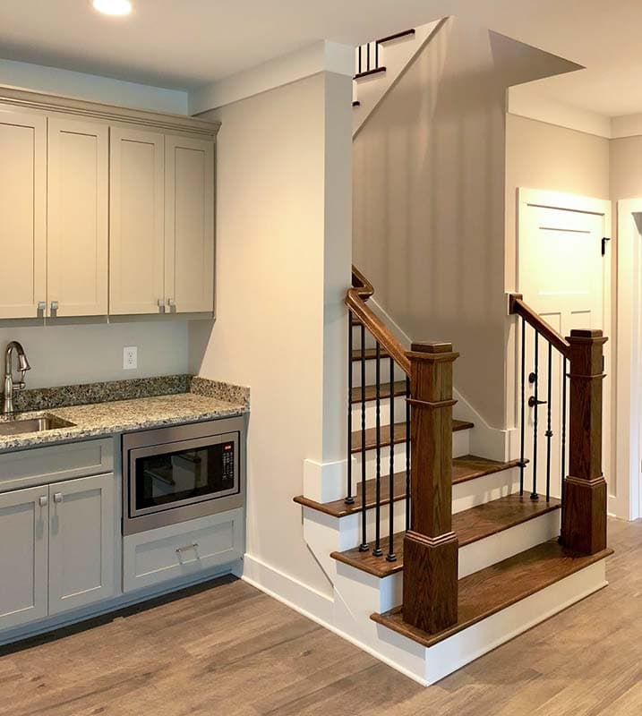 Interior view of a home featuring a wet bar with sink and microwave, adjacent to a wooden staircase with metal balusters.