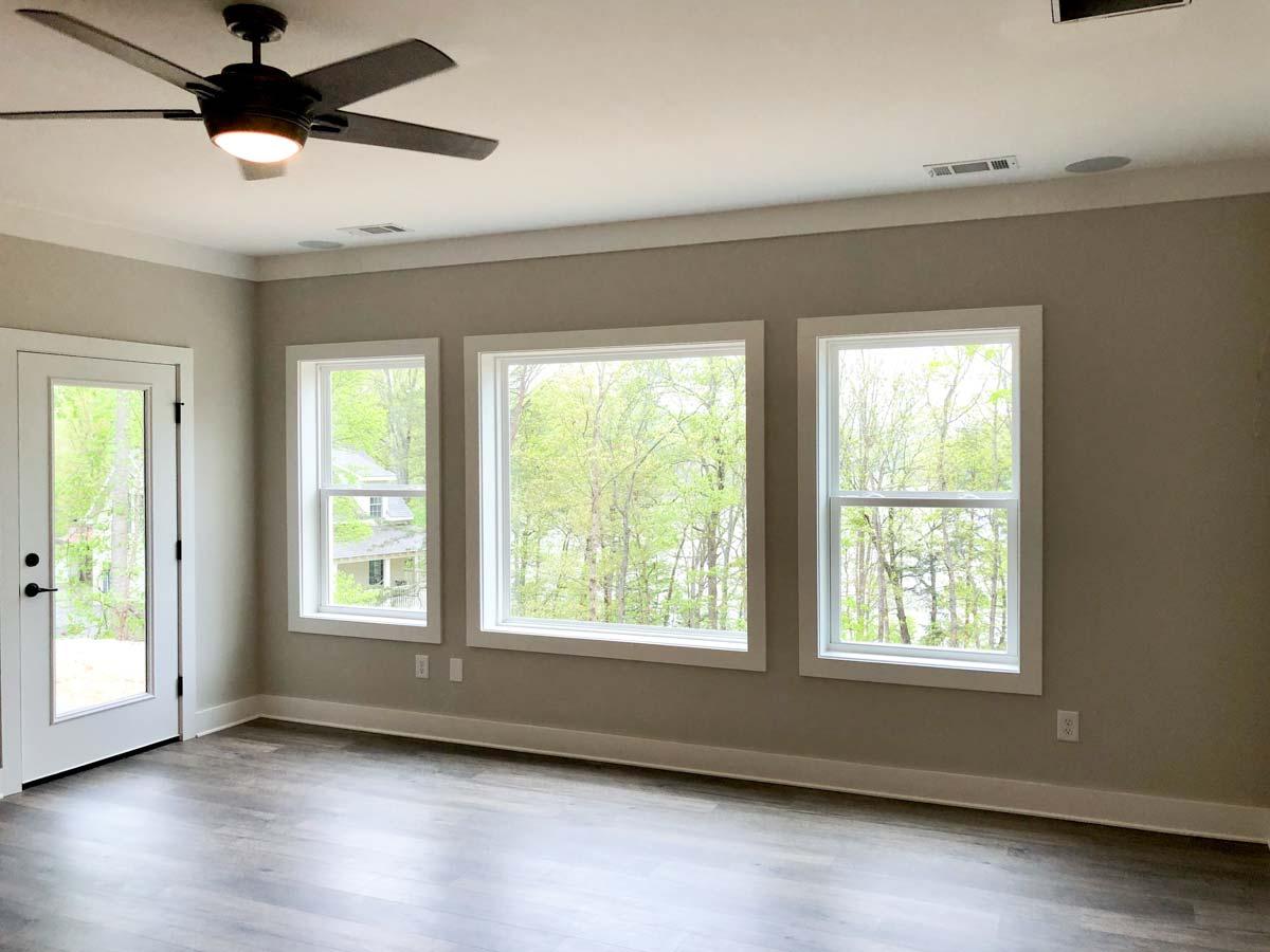 Interior view of a room with a ceiling fan, a door, and three windows overlooking trees and houses.