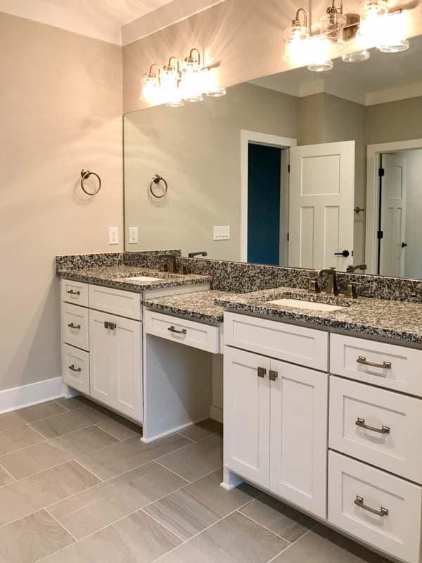 Double vanity with granite countertops, white Shaker cabinets, and a built-in makeup area.