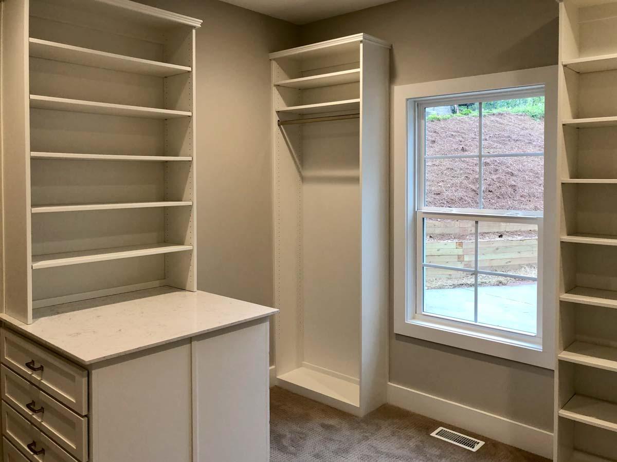 Walk-in closet with built-in shelving, counter, and hanging rod. Window shows exterior slope.