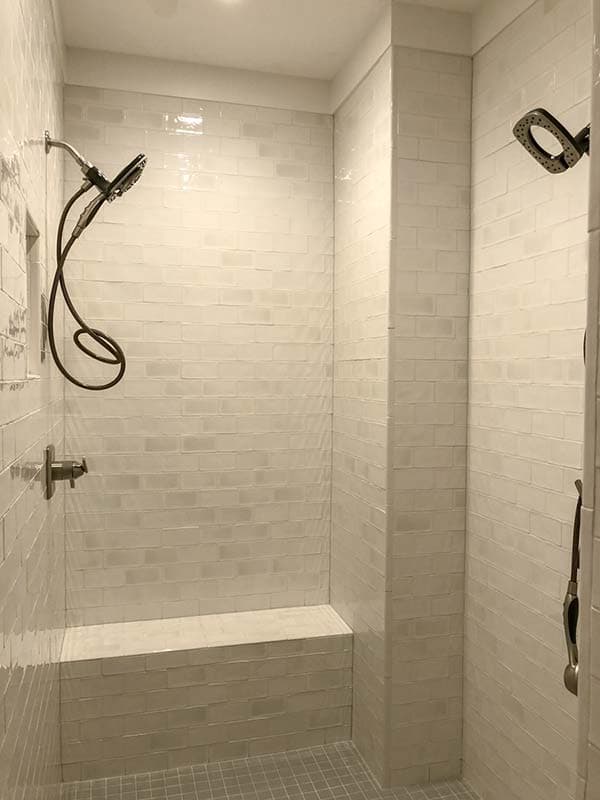 Tiled shower with built-in bench, handheld showerhead, and dual showerheads.
