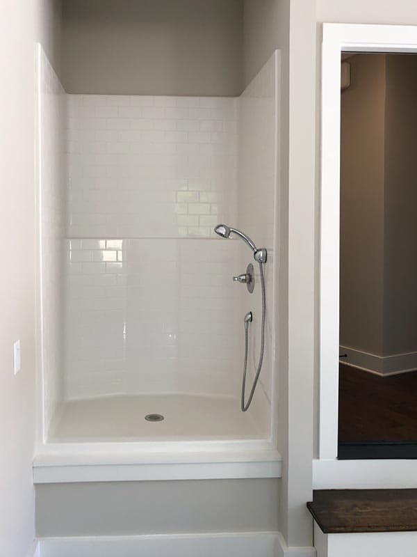 White subway tile shower with a built-in bench, handheld showerhead, and a curved base.