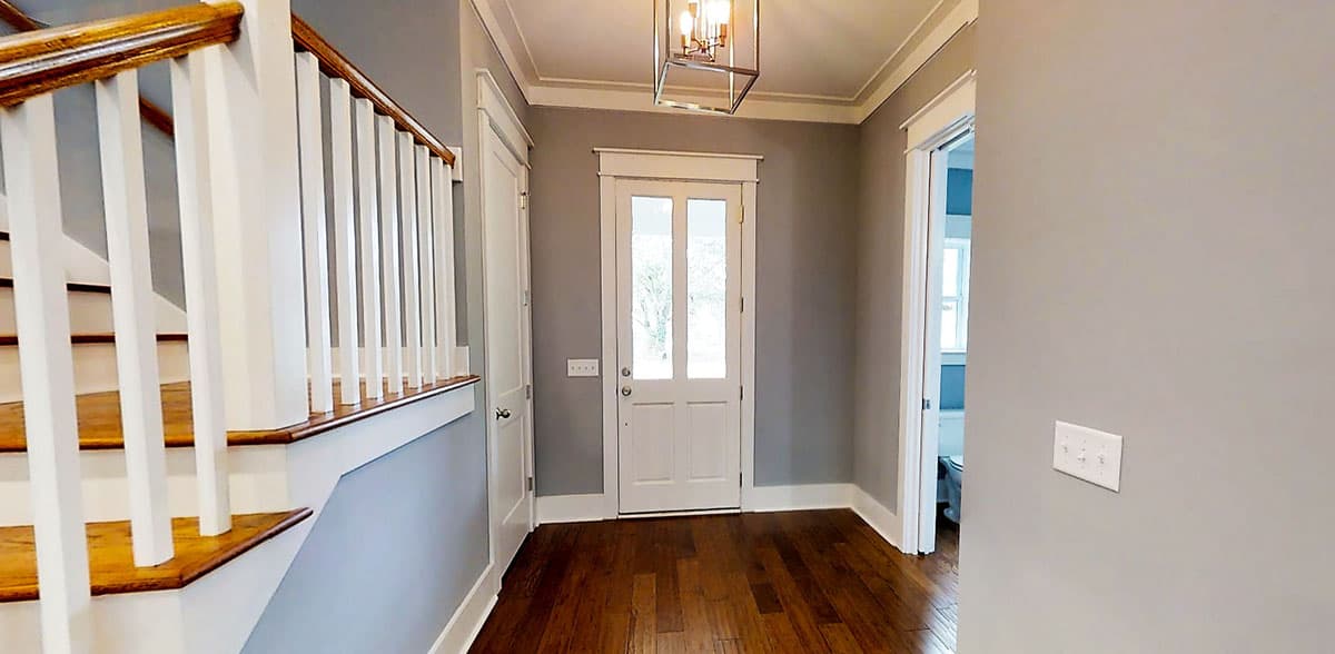 Interior view of a house foyer with a staircase, paneled door, and overhead light fixture.