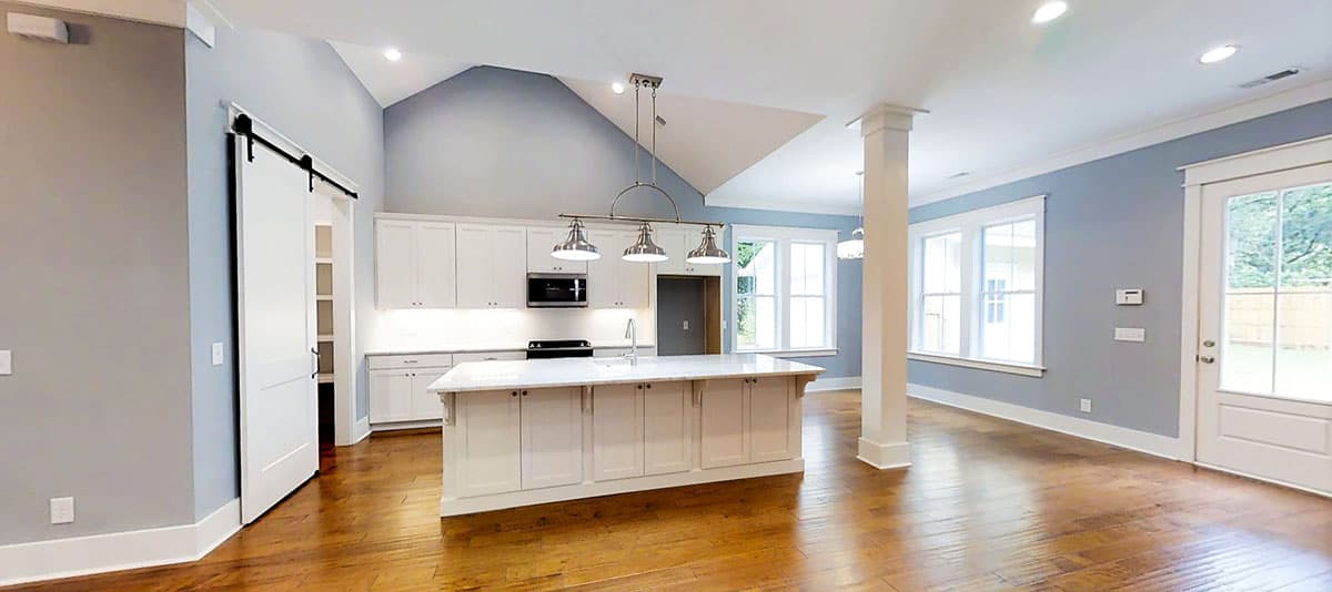 Interior rendering of an open-concept kitchen and living area with vaulted ceilings, a large island, white cabinetry, and a barn door.