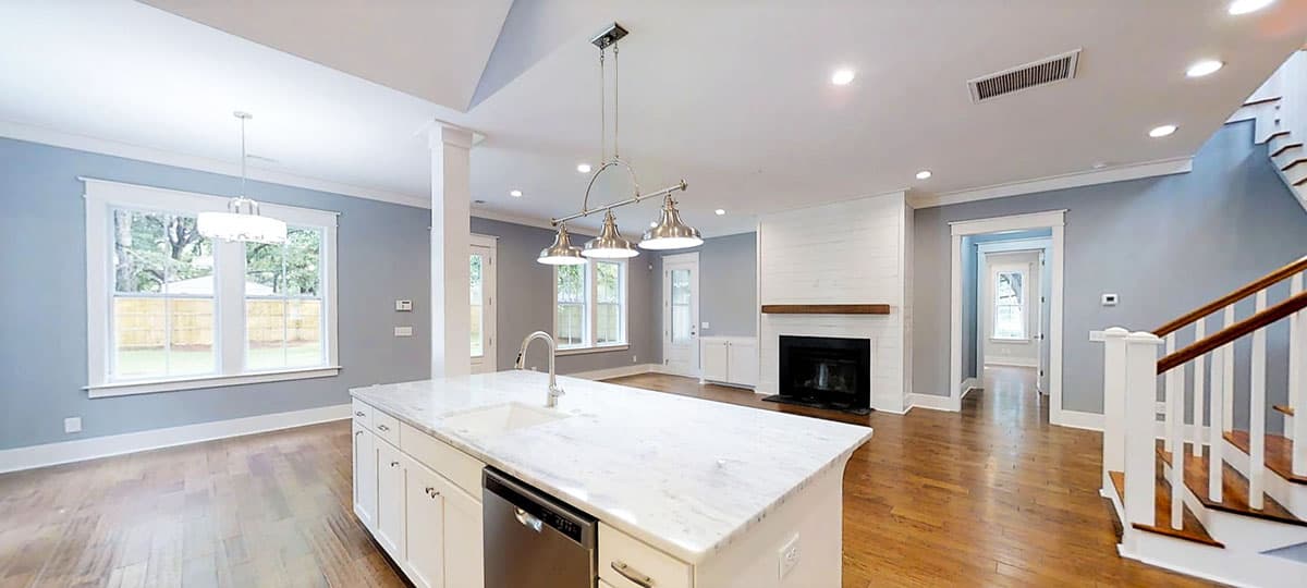 Interior view of a house showing a large kitchen island with sink, fireplace, and staircase. Open layout.