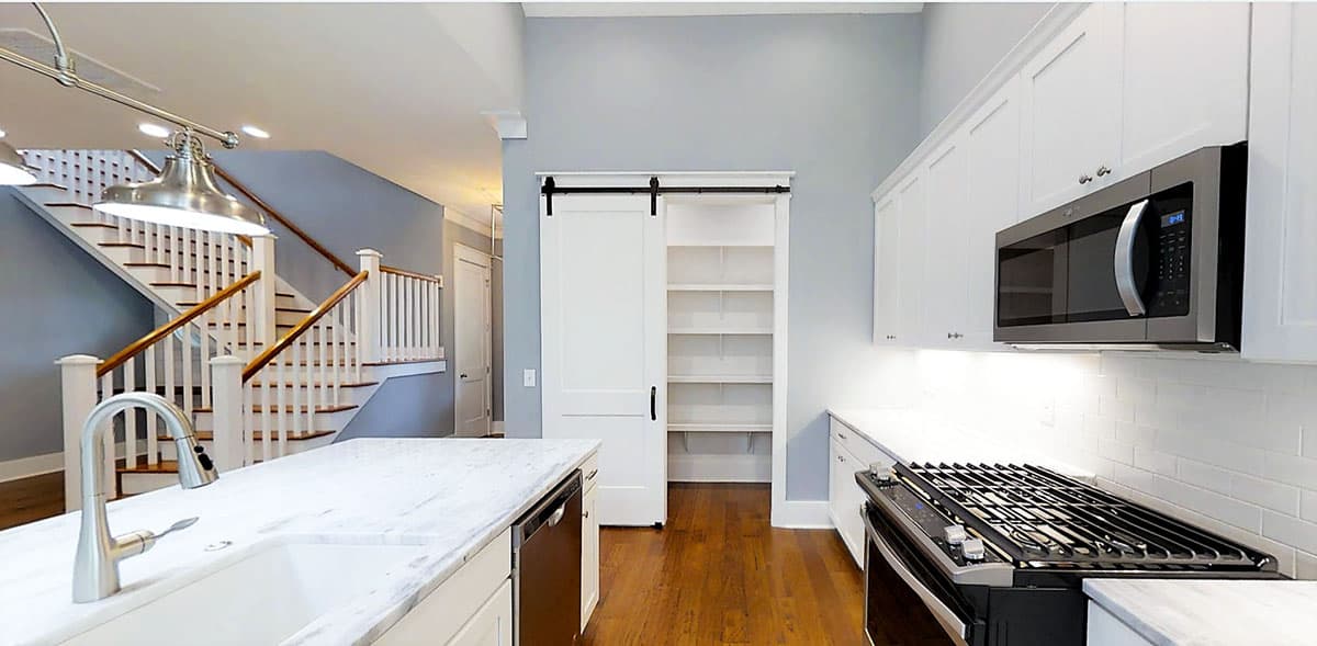 Interior view of a kitchen with a marble island, white cabinets, a sliding barn door pantry, and a staircase.