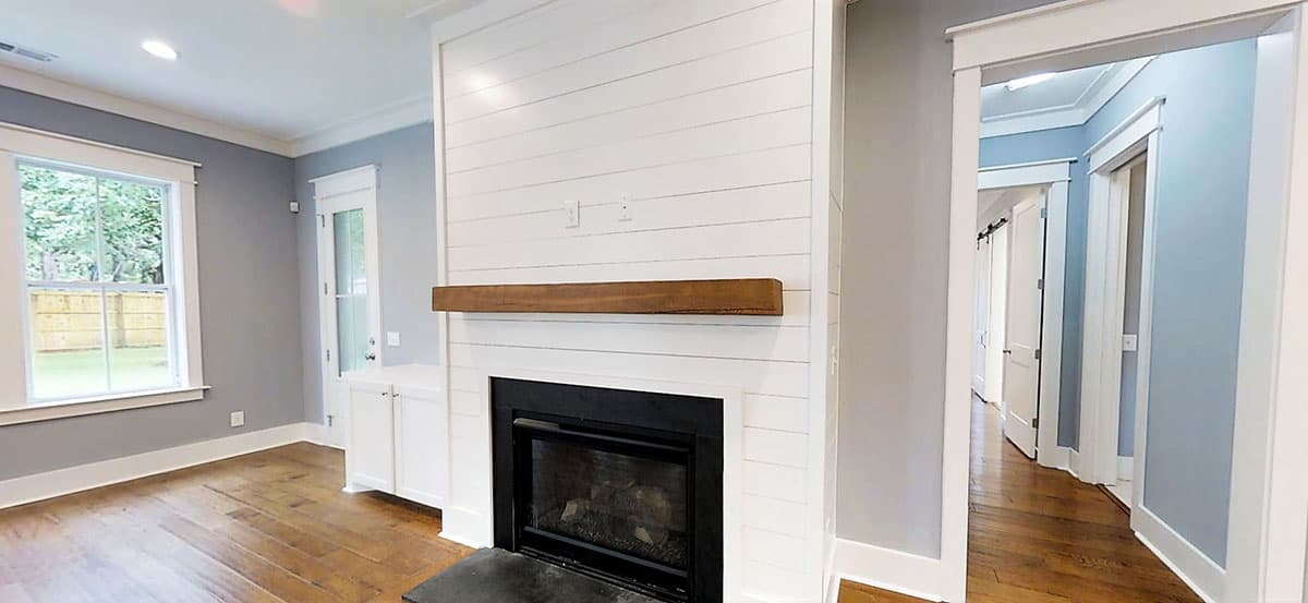Living room interior with shiplap fireplace, wood mantel, built-in cabinets, and hallway view.