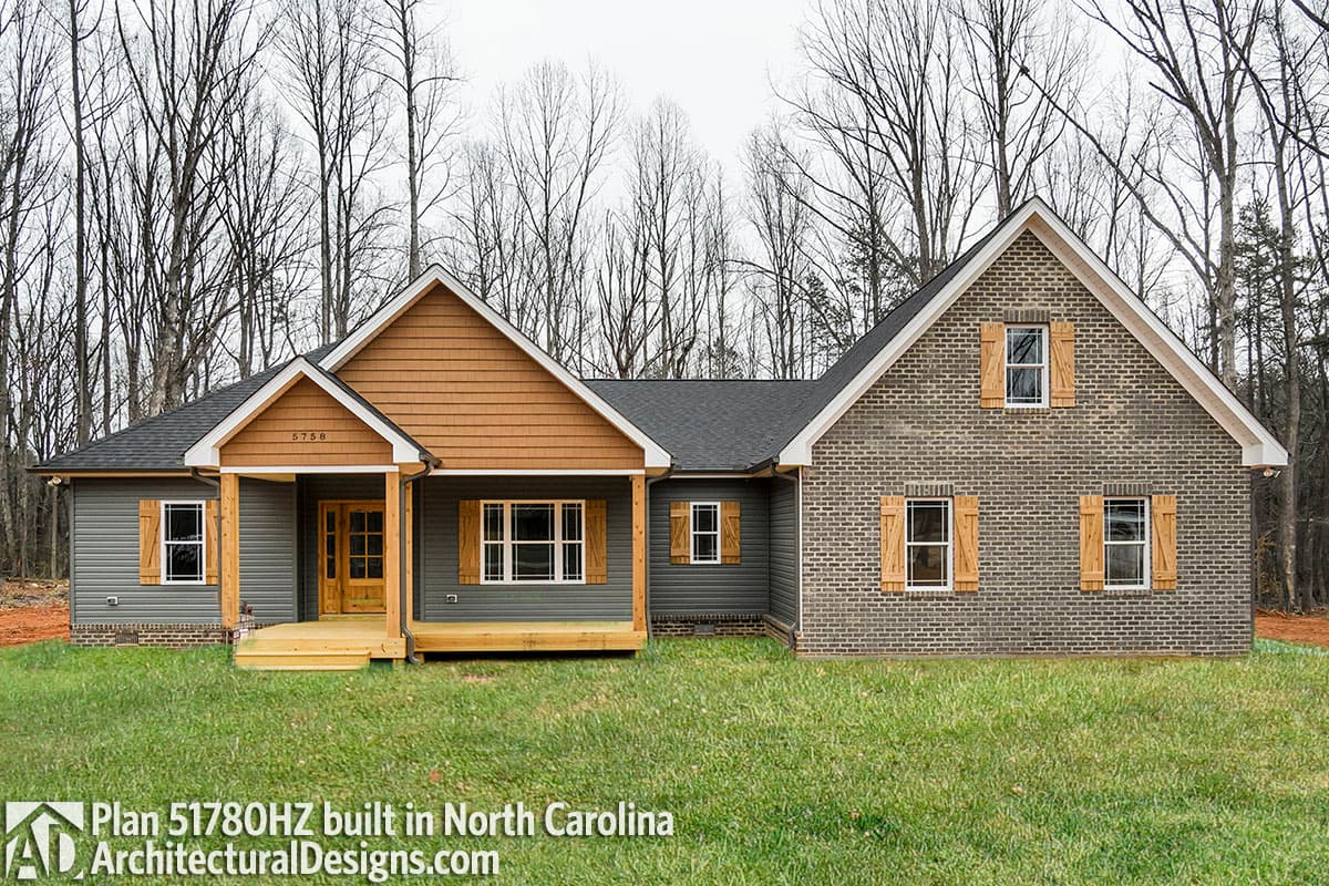 House plan exterior, single-story, with a prominent gabled entrance porch, wood siding, and brick facade with wood shutters.