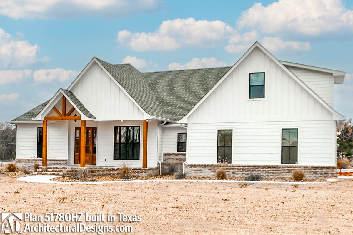 House plan exterior: Modern Farmhouse style, two stories, gabled roof, wood-framed entryway, brick foundation.