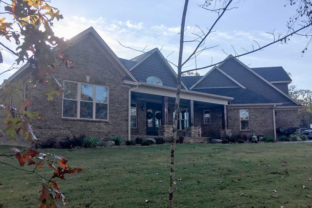House plan exterior featuring a brick facade, prominent front porch with stone columns, and multiple gables.