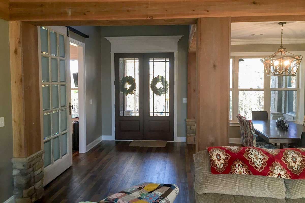 Interior view of a house entry with double doors featuring glass panes and wreaths. Features wood beams and a sliding barn door.