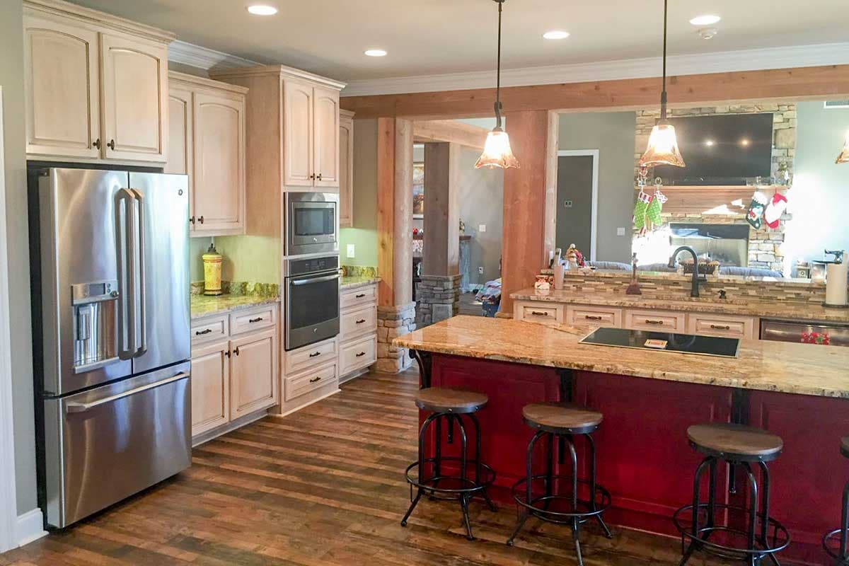 Kitchen with stainless steel refrigerator, double ovens, granite countertops, and a red island with bar stools.