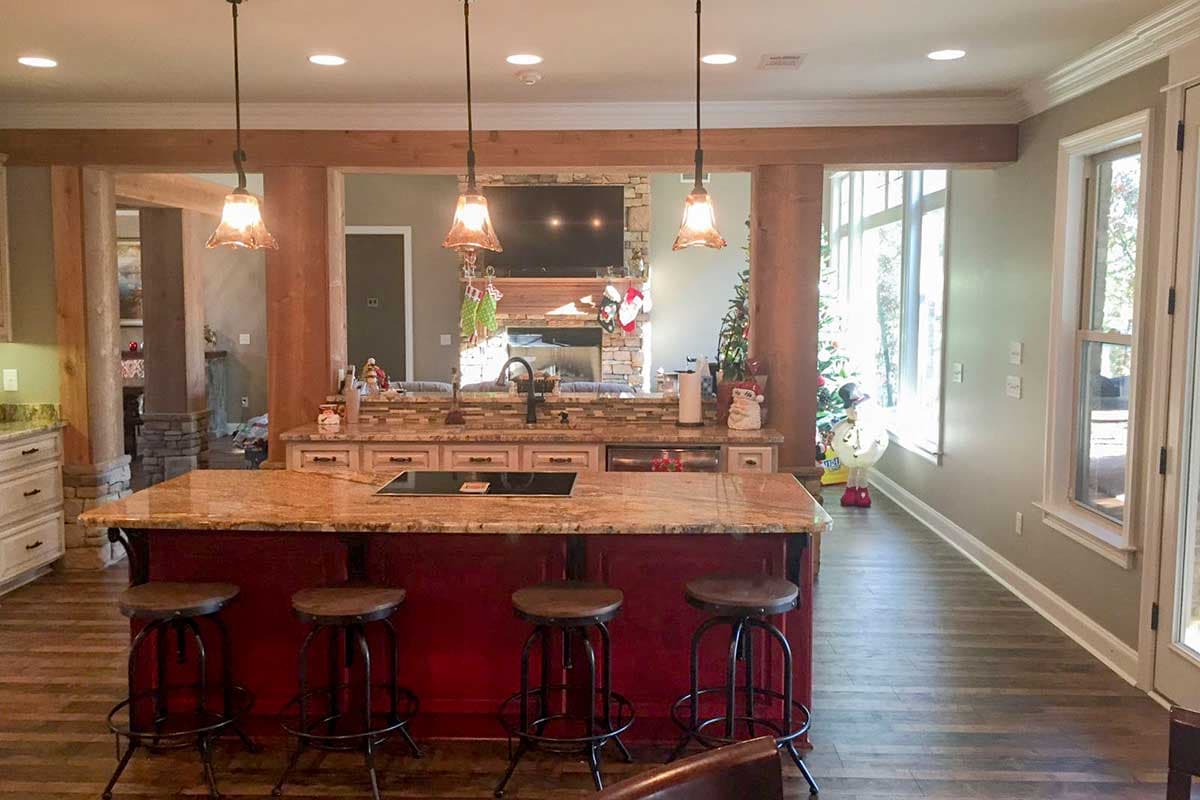 Open-concept kitchen with large island, stone fireplace, and wood beam accents visible through structural columns.