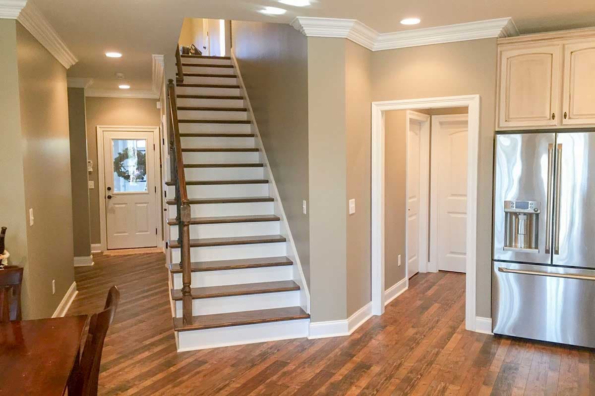 Interior view of a house interior with a staircase, wood flooring, and stainless steel refrigerator.