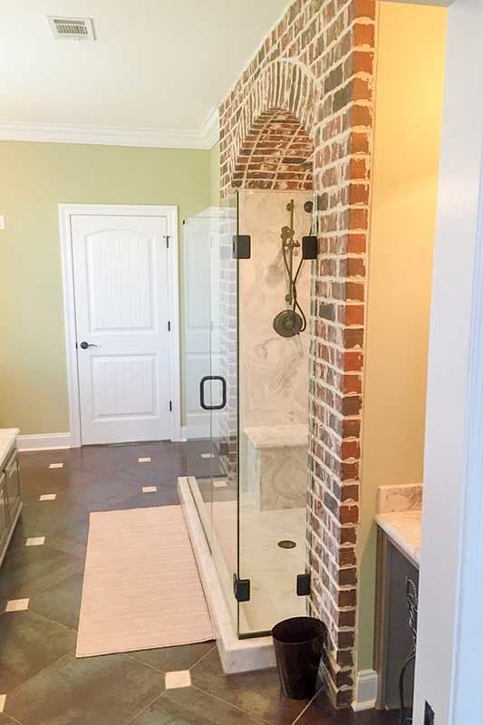 Bathroom interior featuring glass-enclosed shower with arched brick accent wall, marble tile, and white door.
