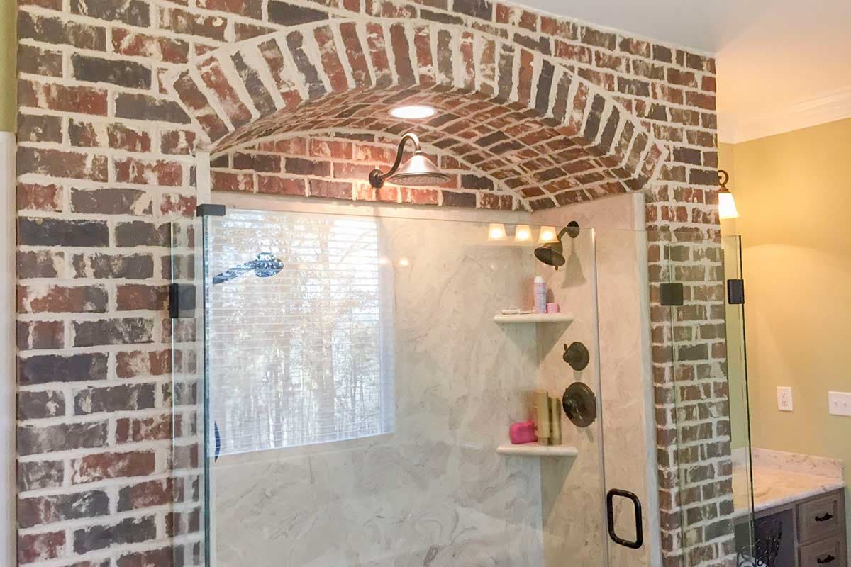 Bathroom shower with glass enclosure, brick arch ceiling, dual shower heads, and marble-look tile walls.