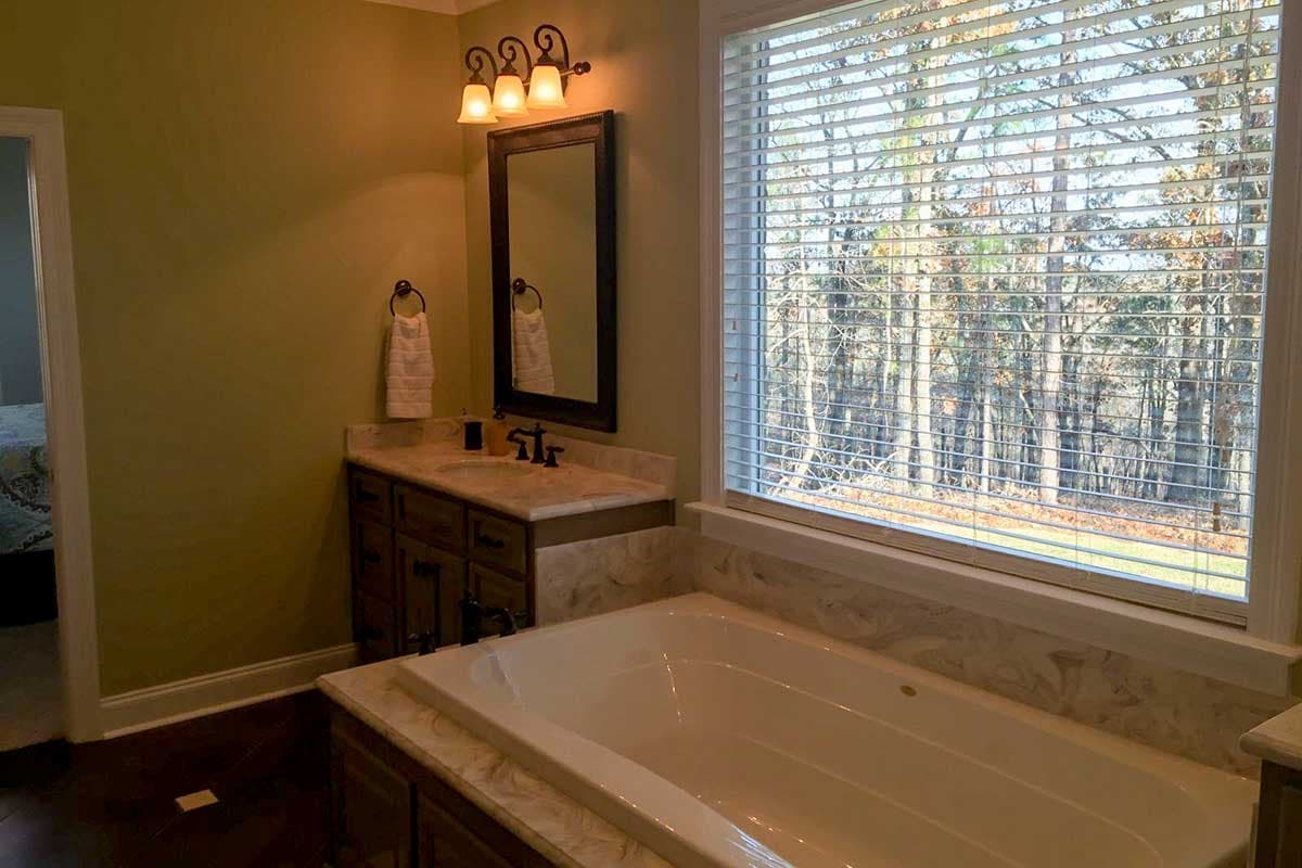 Bathroom interior with a dual vanity, large soaking tub, and a wide window overlooking a wooded area.