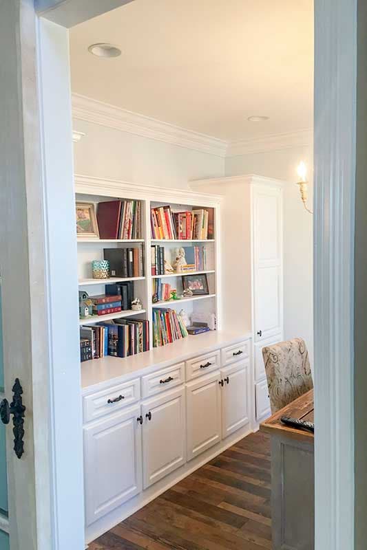 Built-in white bookcases and cabinetry with a desk and chair to the right.