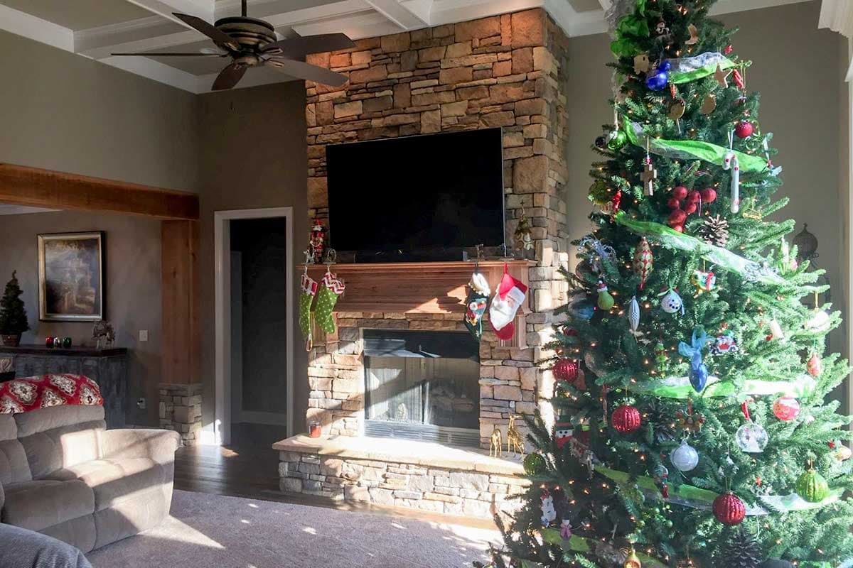 Living room with coffered ceiling, fan, stone fireplace, mantel, and Christmas tree.