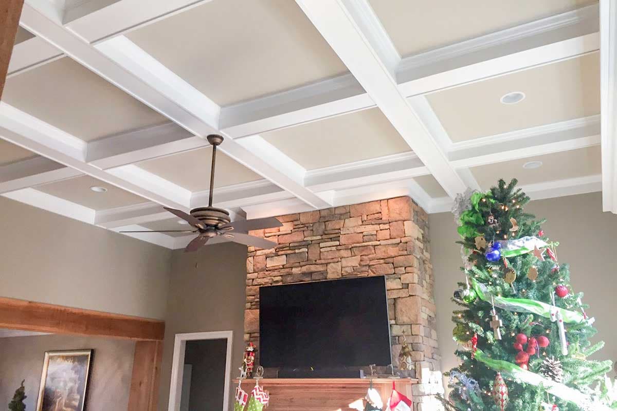 Coffered ceiling with recessed lighting and a ceiling fan above a stone fireplace and television.