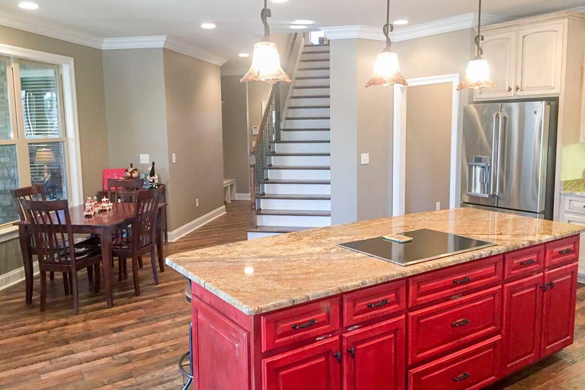Interior view of a kitchen with a red island, dining area, and staircase. Features include granite countertops and stainless steel appliances.