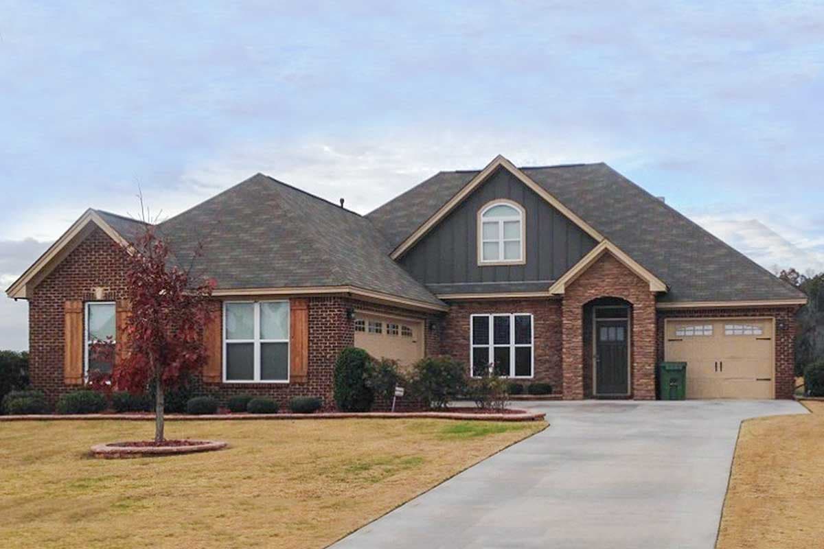 House plan exterior with brick facade, front-facing garage, and multiple gables. Features include dormers and a stone-covered entry.