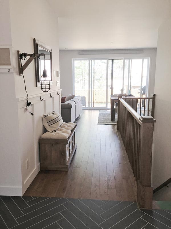 Interior view of a house entryway with wooden floors, a bench, and sliding glass doors leading to an outdoor area.
