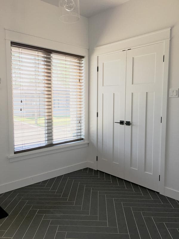 Interior view showing double doors with paneling, a window with blinds, and dark gray herringbone tile flooring.