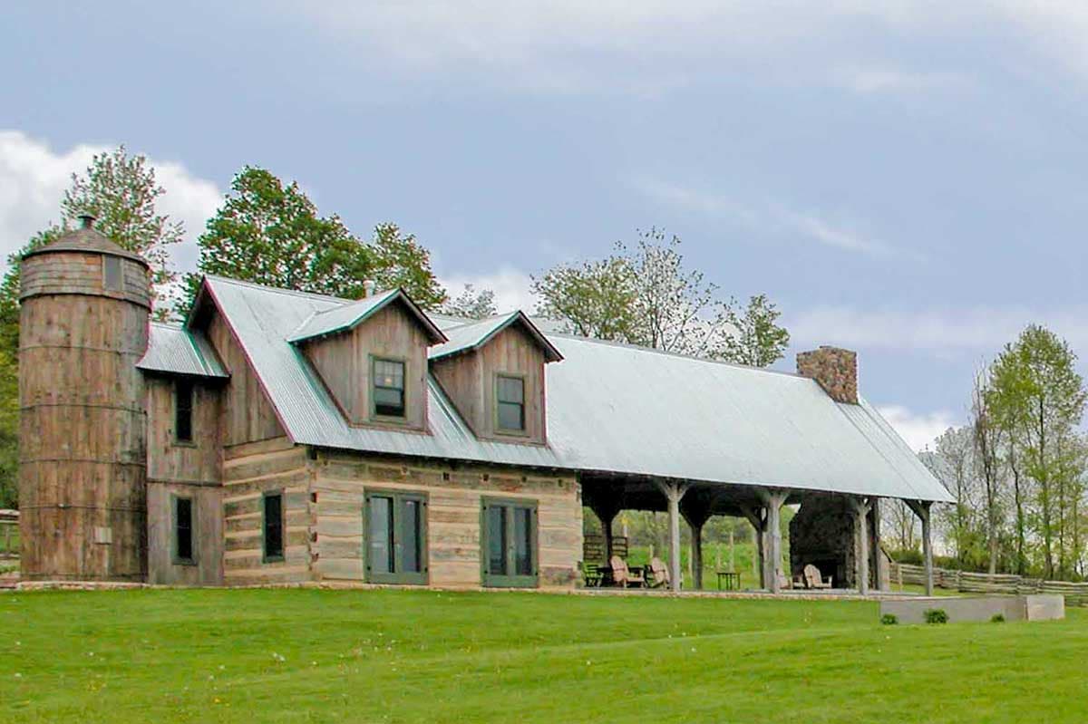 House plan exterior. Rustic style home with two stories. Features include a silo, dormers, a covered porch, and a stone chimney.