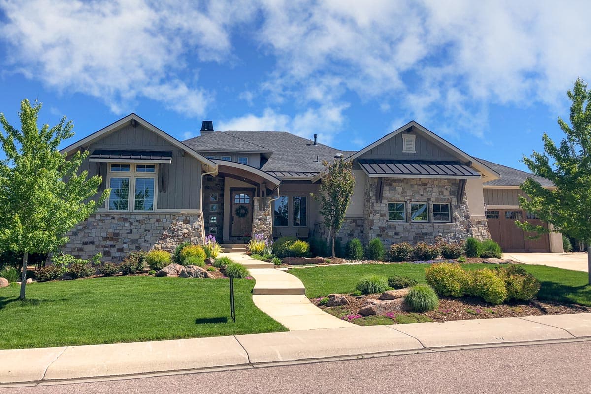 House plan exterior featuring stone accents, gabled rooflines, and a covered entry. Includes an attached garage with carriage-style doors.