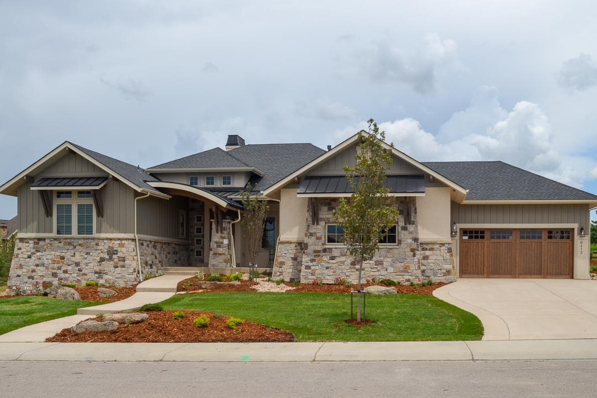 House plan exterior with stone and siding, multiple gables, metal awnings, and a three-car garage.