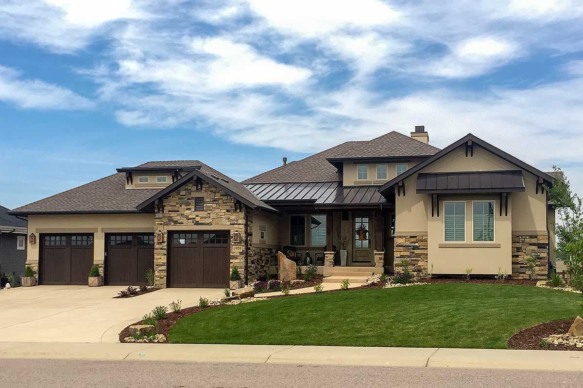 House plan exterior with stone accents, dark metal awnings, and a mix of gable rooflines. Features a three-car garage and entry porch.