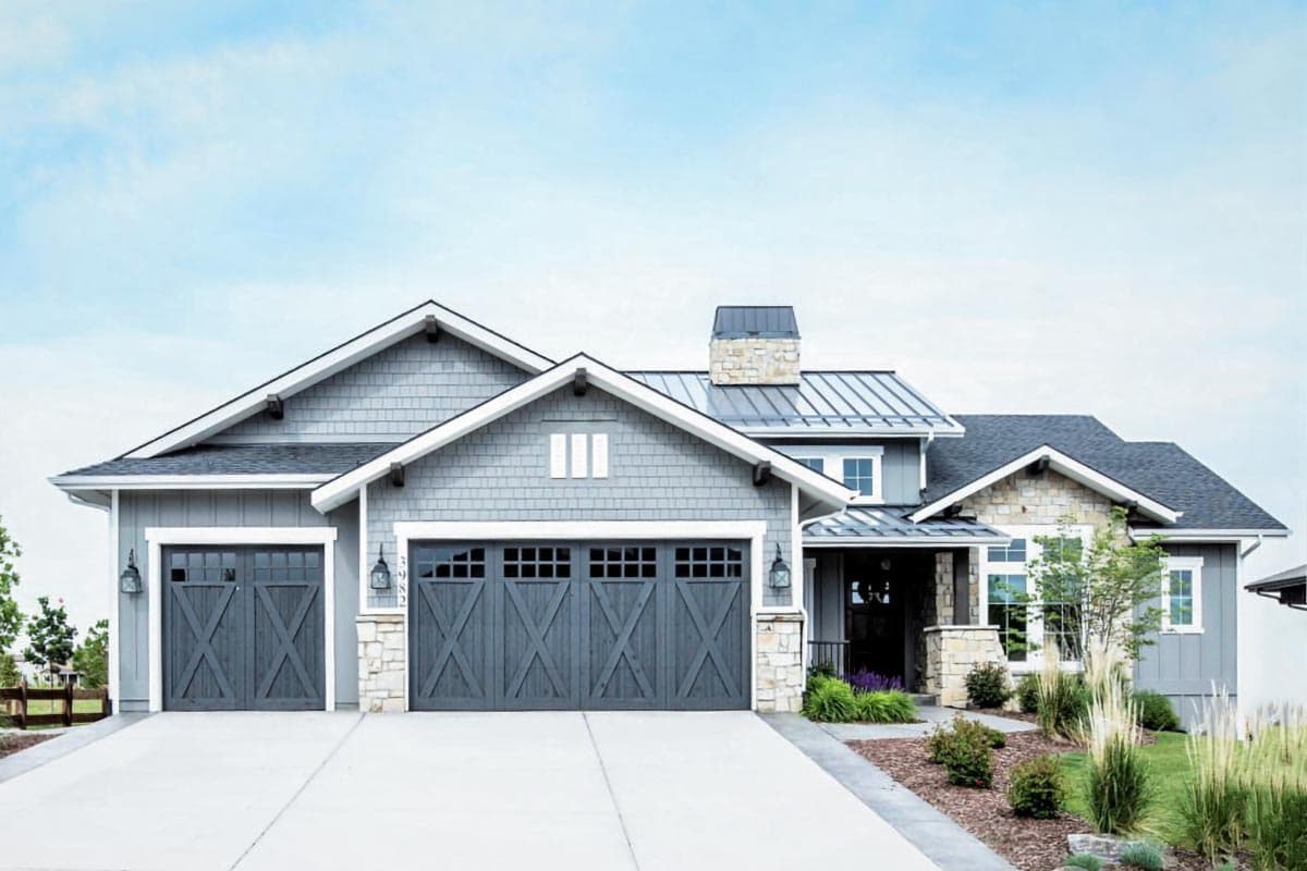 House plan exterior. Craftsman style with two stories, gabled rooflines, stone accents, and carriage-style garage doors.